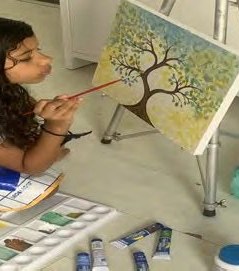 Aluna pintando uma árvore em tela no cavalete