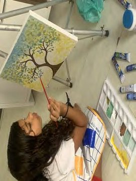 Aluna pintando uma árvore em tela no cavalete