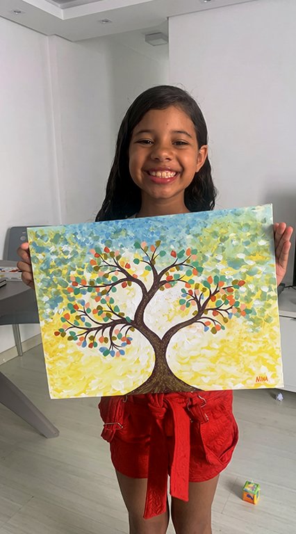 Aluna criança sorridente mostra sua pintura de árvore colorida